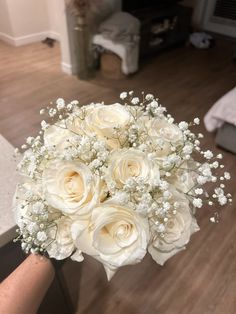 a bouquet of white roses and baby's breath is held in someones hand