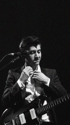 a man in a suit and tie holding a guitar while standing next to a microphone