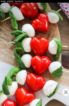 some red and white hearts are on skewers with green leafy leaves around them