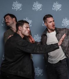 three men standing next to each other in front of a comic con panel wall with their mouths open