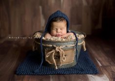 a newborn baby in a bucket is posed for a photo while wearing a bonnet and sleeping