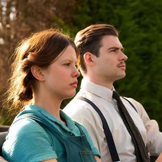 a man and woman sitting next to each other on a park bench looking off into the distance