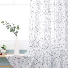 a white vase sitting on top of a wooden table next to a window covered in curtains