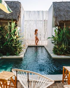 a woman standing in the middle of a swimming pool surrounded by greenery and chairs