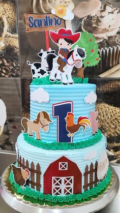 a three tier cake with farm animals and barnyard decorations on the top is decorated in blue icing