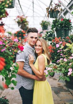 a man and woman standing next to each other in a greenhouse with lots of flowers