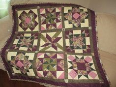 a purple and green quilt sitting on top of a couch next to a white pillow