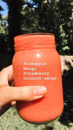 a person holding up a red mason jar with the words pineapple mango strawberry coconut water