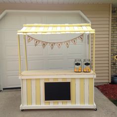 a small yellow and white food stand with bunting on the roof, decorated with mason jars