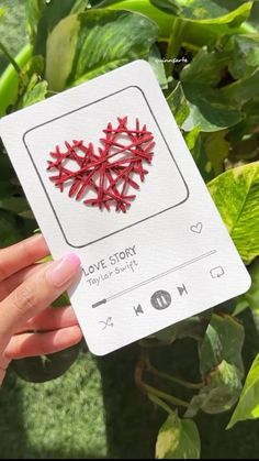 someone holding up a card with a red heart on it in front of some plants