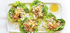 four lettuce wraps with shredded cheese and carrots on top, sitting on a white plate