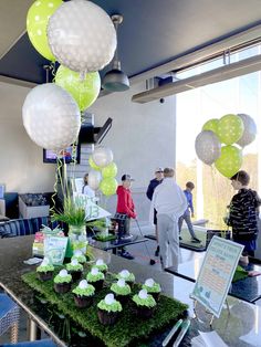 some people are standing in a room with balloons and cupcakes on the table