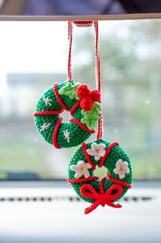 two crocheted christmas wreaths hanging from a window sill in front of a car