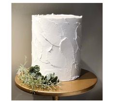 a white cake sitting on top of a wooden table next to a potted plant