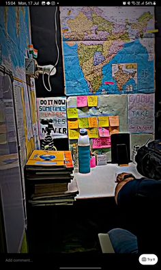 a person sitting at a desk in front of a wall covered with posters and post - it notes