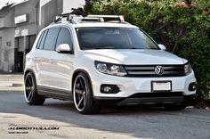 a white volkswagen suv parked in front of some bushes