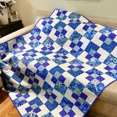 a blue and white quilt sitting on top of a couch next to a vase with flowers