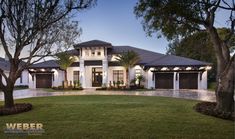 a large white house with two garages and trees in the front yard at dusk