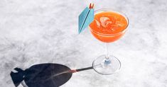 an orange drink in a wine glass with a blue umbrella on the top and shadow