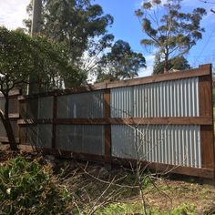 a fence made out of corrugated steel and wood with trees in the backgroud