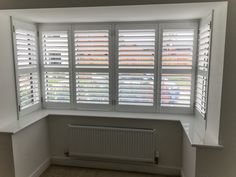 an empty room with white shuttered windows and radiator in the corner,