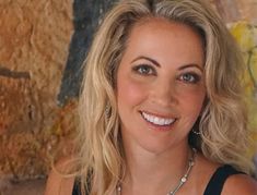 a woman with blonde hair wearing a black top and silver necklace smiling at the camera