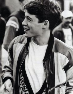 black and white photograph of a young man in a leather jacket smiling at someone behind him