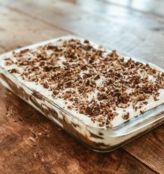 a dessert in a glass dish on top of a wooden table with white frosting and chocolate shavings