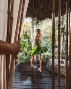 a woman in a green dress is standing on a wooden platform with palm trees behind her