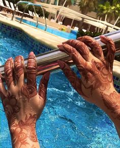 two hands with henna on their arms near a swimming pool holding onto a pole