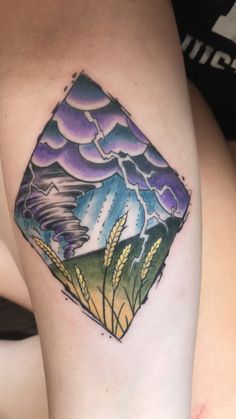 a woman's leg with a tattoo on it that has an image of mountains and clouds in the sky