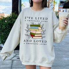 a woman is holding a coffee and wearing a sweatshirt that says i've lived a thousand lives and loved a thousand loves