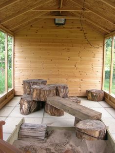 the inside of a wooden building with benches and logs on the ground in front of it