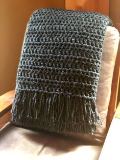 a gray crocheted blanket sitting on top of a chair next to a pillow