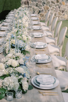 a long table with white and blue flowers is set for an outdoor dinner party or reception