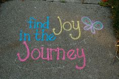 the words find joy in the journey written with colored chalk on pavement next to flowers