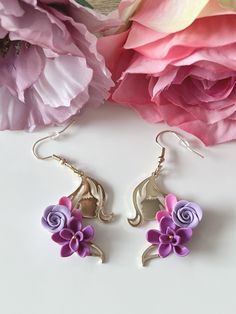 purple and pink flowers are hanging from silver earwires on a white surface next to large pink flower petals