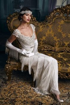 a woman sitting on top of a chair wearing a white dress and tiara with fringes