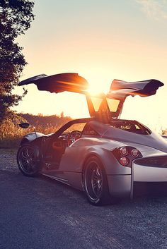 a silver sports car with open doors parked on the side of a road at sunset