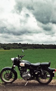 a motorcycle parked on the side of a dirt road in front of a green field