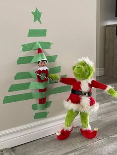 an elf and the grinch are standing next to a christmas tree