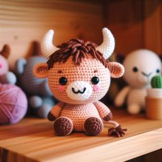 a crocheted stuffed animal sitting on top of a wooden table next to balls of yarn