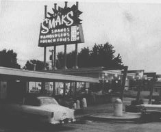 an old black and white photo of people at a gas station with cars parked in front