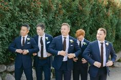 a group of men standing next to each other wearing suits and ties with their hands in their pockets