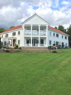 a large white house sitting in the middle of a lush green field with stairs leading up to it