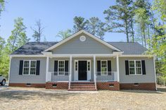 a gray house with black shutters on the front porch and red brick steps leading up to it