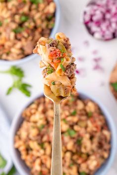 a spoon full of food on top of a bowl with other bowls in the background