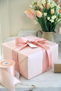 a pink gift box sitting on top of a table next to a vase filled with flowers