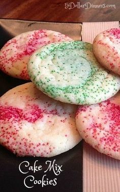 four decorated cookies sitting on top of a black plate with red, green and white sprinkles