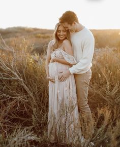 a pregnant couple standing in tall grass at sunset